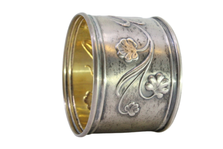 Argola de guardanapo em prata com figura de jovem e motivos florais relevados.